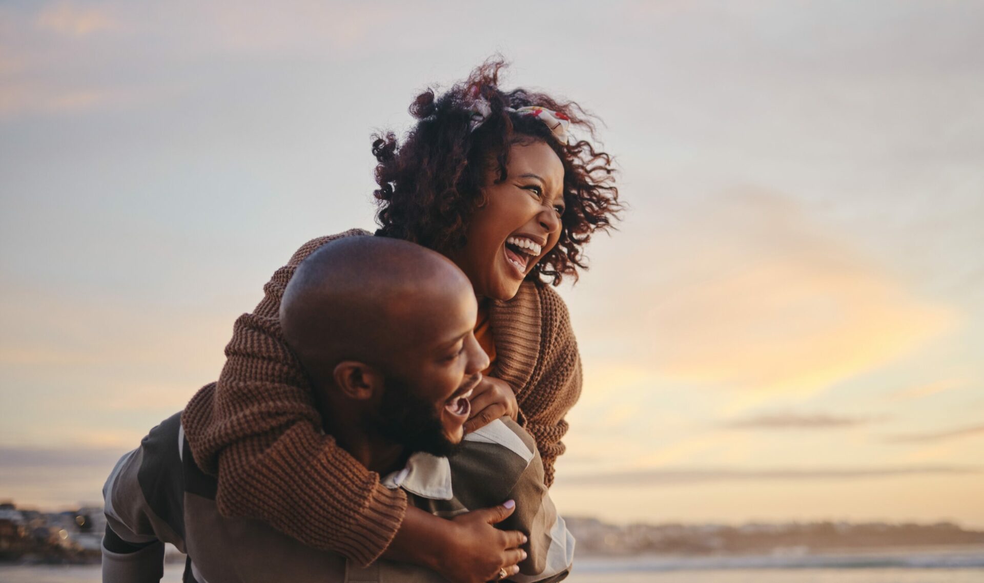 Un couple souriant et s'amusant ensemble sur une plage au coucher du soleil, reflétant joie et complicité.